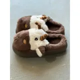 Pantuflas de peluche con diseño de vaca, confeccionadas en piel sintética suave. Cuentan con suela de goma antideslizante y diseño abierto en el talón.