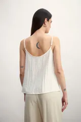 Musculosa color blanco roto con escote en V y botones frontales. La tela presenta una textura arrugada o plisada.