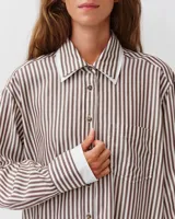Camisa de corte recto y silueta fluida, con estampado a rayas marrones y blancas. Presenta cuello clásico, cierre frontal con botones y un bolsillo aplicado en el pecho. Las mangas largas son ligeramente abullonadas, con puños ajustados que aportan volumen a la prenda.