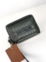 Mini billetera de cuero con textura efecto cocodrilo y cierre perimetral. Presenta un parche central con el logo de la marca grabado.