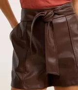 Short corto color marrón oscuro, confeccionado en poliuretano (PU) con textura que imita el cuero. Presenta cintura elástica en la parte trasera, lazo delantero para ajustar y recortes decorativos.