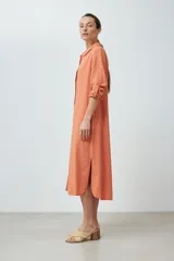 Vestido camisero midi color durazno, de lino, con cuello camisero, abotonado al frente y mangas largas con trabillas.