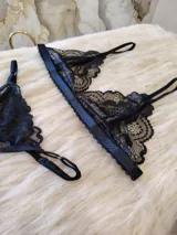 Conjunto de lencería compuesto por un bralette de encaje con breteles regulables y una tanga regulable con corte cola less. Ambas piezas presentan un diseño de encaje floral negro.