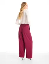 Pantalón tipo palazzo de corte ancho y fluido, confeccionado en tejido sastrero. Presenta tiro alto con doble abotonadura frontal, pinzas decorativas y cintura elástica en la parte posterior. Incluye bolsillos laterales funcionales.