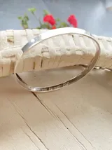 Esclava rígida de plata con diseño de cinta lisa y grabado personalizado en su cara interna.