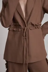 Blazer negro con solapas de muesca, corte holgado, cierre frontal con lazo y detalle de volados en los bolsillos.