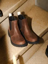 Bota tipo chelsea de cuero marrón con textura granulada, paneles elásticos laterales en color negro y suela track dentada de goma negra.