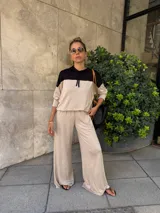 Sudadera con capucha de manga larga, color beige, con canesú negro en la parte superior de los hombros y capucha negra. Presenta cordones negros para ajustar la capucha.