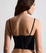 Corset de media copa en color blanco, confeccionado con paneles de poliamida y detalles decorativos de encaje floral en el borde superior y tul en los laterales. Cuenta con tirantes finos ajustables y varillas internas para estructura.