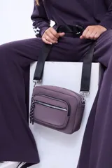 Bandolera de diseño compacto en color beige, con compartimento principal y bolsillo frontal, ambos con cierre. Incluye correa larga regulable y detalle de tirador con cordón en el cierre frontal.