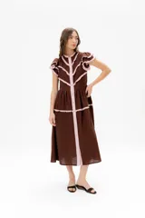 Vestido midi de lino color marrón con detalles de volados en color rosado en las mangas y a lo largo de la parte frontal. Presenta cierre frontal con botones, cuello redondo y diseño de falda amplia.