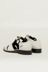 Sandalia cerrada tipo pescador, color blanco o hueso brillante, con tiras entrecruzadas en el empeine y cierre de hebilla ajustable en el lateral. Posee suela y taco bajo de color negro.