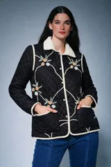 Campera acolchada de color negro con diseño capitoneado, cuello de corderito en color crema y bordados florales en el frente. Posee cierre frontal con botones a presión, bolsillos delanteros y ribetes en color crema.