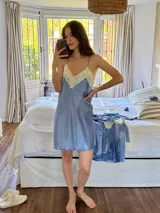 Camisón azul de satén elastizado, con escote en V en la parte delantera y trasera, decorado con puntilla color crema. Los breteles son finos y se cruzan en la espalda.