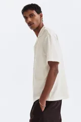 Camisa de manga corta color blanco hueso, de punto jacquard en mezcla de algodón, con cuello abierto y cierre frontal de botones.