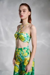 Top strapless con estampado floral en tonos verde y amarillo, con tirantes finos al cuello y detalle de nudo en el centro del busto.