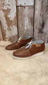 Zapatos de cuero marrón con cordones blancos, suela blanca y detalles de pelo en el lateral.