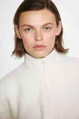 Campera deportiva de sherpa en color blanco, de corte holgado, con cuello elevado, cierre frontal y bolsillos laterales.
