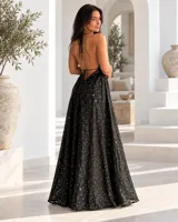 Vestido largo color dorado, confeccionado en tela semitransparente con diseño bordado floral y detalles de brillo. Presenta escote en V, tirantes finos ajustables con borlas en los hombros, y corte amplio y fluido con gran movimiento.