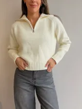 Sweater de tejido de punto color crema, con cuello alto tipo polo y cierre frontal parcial. Presenta mangas largas con puños acanalados y terminación acanalada en la cintura.