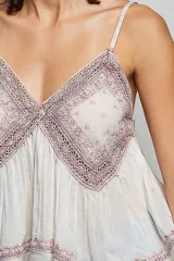 Top de algodón color rosado, con escote en V, tirantes finos, detalles de encaje bordado en el pecho y bajo asimétrico fluido.