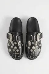 Mocasines negros de cuero sintético estilo zueco, con hebilla lateral plateada y apliques metálicos estilo western en toda la capellada.
