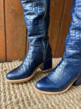 Botas altas de cuero azul marino con textura tipo cocodrilo, taco cuadrado forrado y cierre metálico lateral a lo largo de la caña.