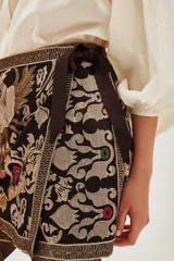 Falda corta tipo portafolio de gabardina liviana, color negro, con bordados florales y de ave en tonos dorados, rosados y morados. Posee un lazo lateral para atar.