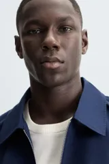 Cazadora bomber azul marino de corte regular fit, confeccionada en tejido de algodón. Presenta cuello solapa, manga larga con puño ajustable de botón, bolsillos de vivo en la cadera, bolsillo interior y bajo con elástico. Cierre frontal con cremallera.