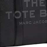Bolso tipo tote de gran tamaño, confeccionado en cuero negro con textura granulada. Presenta el logo de la marca estampado en el frente con la inscripción The Tote Bag Marc Jacobs. Cuenta con asas superiores resistentes y un diseño espacioso.