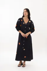 Vestido largo blanco de algodón con bordados de motivos marinos en tonos naranja, verde y azul. Tiene escote en V, mangas 3/4 abullonadas y cierre frontal con botones.