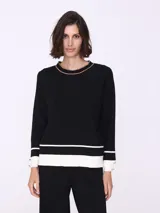 Sweater negro con cuello redondo ribeteado en marrón, corte recto y puños con detalle de botones dorados.