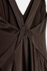 Vestido largo de satén color marrón oscuro, con escote en pico pronunciado, tirantes anchos y bajo en línea evasé con abertura lateral.