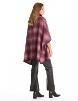 Ruana de tejido suave, color beige y marrón con estampado geométrico repetitivo. Posee cuello con aplique de piel sintética marrón y ribetes negros. Se combina con un suéter marrón de manga larga con botones en el puño.