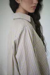 Camisa de rayas verticales rosadas y celestes, con cuello clásico, botonadura frontal y doble bolsillo delantero. Tiene un calce relajado y terminación curva en el ruedo.