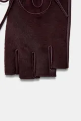 Guantes tipo mitones confeccionados en piel con acabado efecto pelo. Presentan un diseño sin dedos, con una abertura circular en el dorso ajustada mediante una lazada del mismo material.