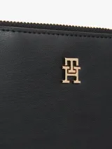 Billetera pequeña de poliuretano negro con acabado granulado. Presenta un compartimento principal con cierre de cremallera y una sección con cierre a presión para tarjetas. Lleva una insignia metálica con el monograma TH en el frente.