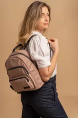 Mochila urbana de diseño funcional en color beige, confeccionada en tela impermeable. Cuenta con un compartimento principal amplio, un bolsillo secundario y un bolsillo frontal, todos con cierre. Incluye asa superior y correas ajustables para los hombros, con detalle de etiqueta de marca en el frente.