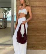 Bolso de hombro tipo hobo color negro, con acabado de gamuza o material similar. Decorado con tachas metálicas redondas plateadas a lo largo del borde inferior y en un dije colgante con forma de corazón.