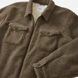 Campera de sherpa color marrón con cierre frontal, cuello camisero y dos bolsillos frontales con solapa y botón. El interior del cuerpo está forrado en franela y las mangas en tafetán.
