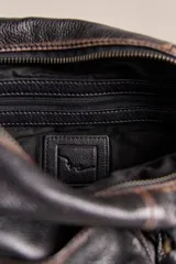 Cartera de cuero verde militar con acabado gastado, cuerpo blando, asas de mano, bolsillos frontales con cierre y tiras colgantes.