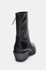 Botín de estilo cowboy confeccionado en piel, con diseño de caña media, puntera fina y tacón medio ancho. Presenta costuras decorativas en el cuerpo y cierre mediante cremallera lateral.