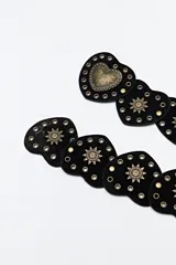 Cinturón negro de cuero sintético compuesto por una serie de piezas en forma de corazón unidas entre sí. Presenta detalles de tachas metálicas doradas y apliques decorativos en forma de sol, con un corazón central de mayor tamaño con diseño grabado.