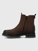 Bota tipo Chelsea de cuero marrón con paneles laterales elásticos en color negro. Presenta costuras reforzadas en el contorno y una suela robusta de poliuretano con base dentada en tono gris translúcido.