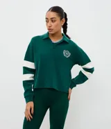 Saco deportivo de modal color verde, con cuello polo, escote en V y mangas largas con franjas blancas horizontales. Presenta un bordado circular en el pecho con la inscripción '94'.