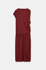 Vestido largo color borgoña, con escote barco y manga caída/sisa. Presenta un drapeado lateral que genera un bajo asimétrico.
