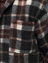 Sobrecamisa de textura tipo teddy con estampado de cuadros en tonos marrón, negro y crema. Presenta cuello camisero, cierre frontal de botones, bolsillos en el pecho y puños abotonados, con un corte relajado.