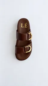 Sandalias de horma anatómica color marrón, confeccionadas en cuero texturado, con dos tiras anchas ajustables mediante hebillas metálicas doradas.