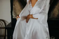 Bata corta de satén elastizado color blanco, con mangas tres cuartos terminadas en volados y lazo ajustable en la cintura.