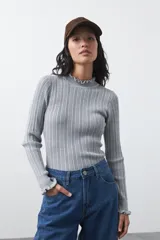 Polera de tejido acanalado gris, con cuello alto y puños con terminación de volados. Presenta un diseño entallado y textura vertical.